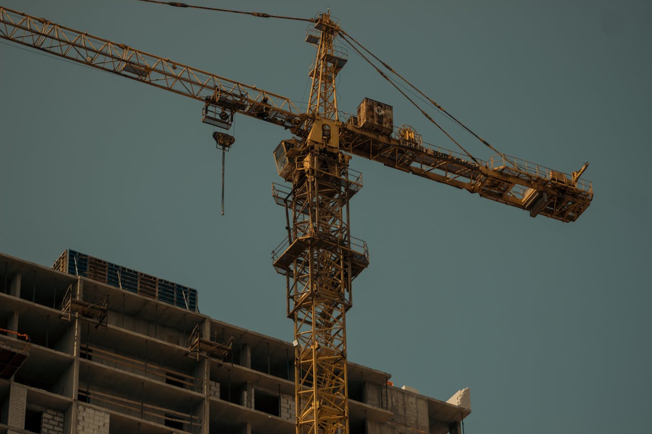 Vertical shot of a tower crane towering above an urban construction site, set against a plain sky.